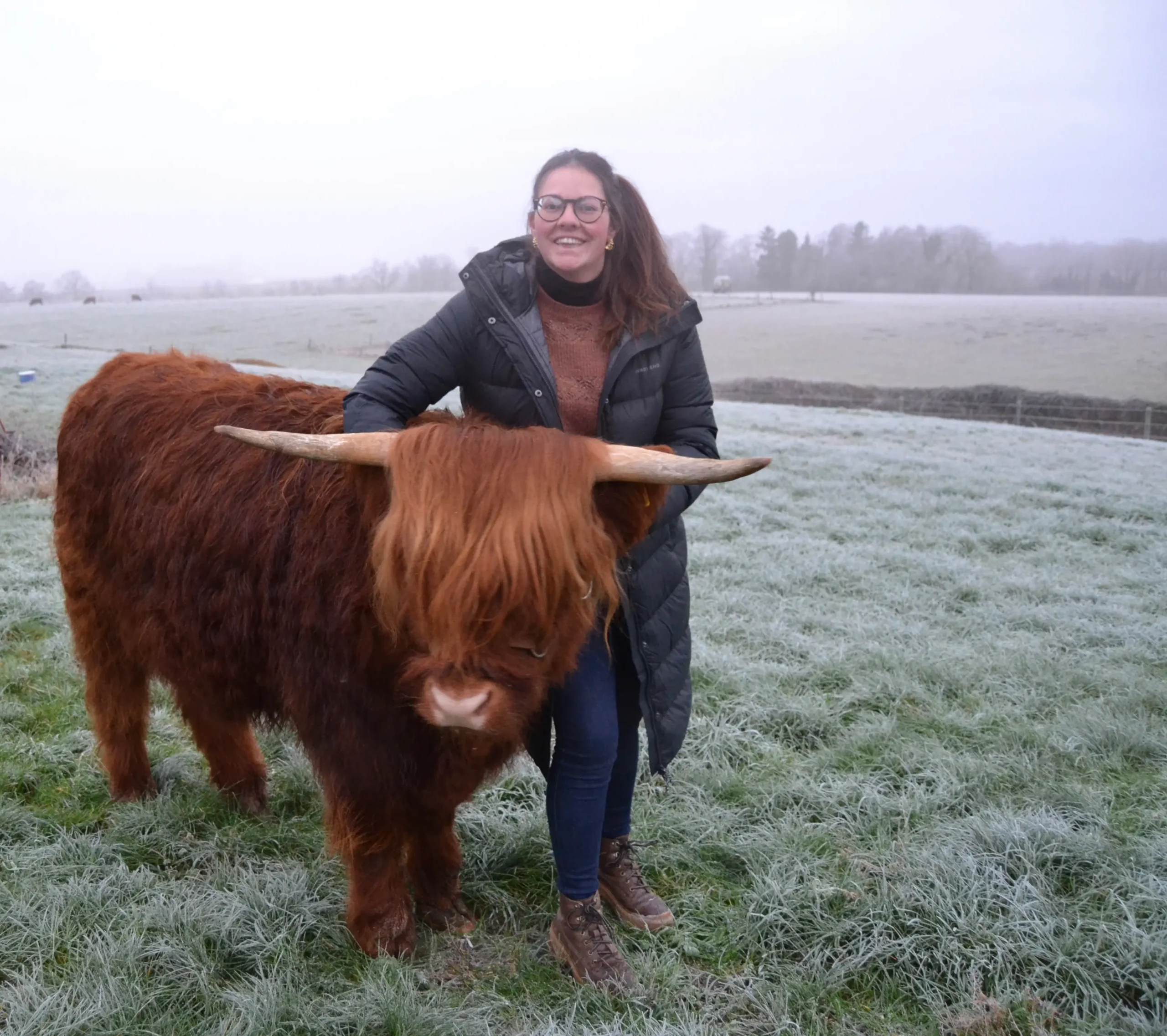 Glimlachende vrouw naast een volwassen Schotse Hooglander in een winters landschap.